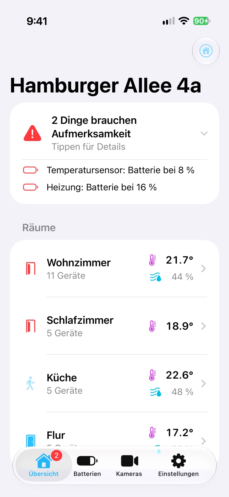Die Übersicht von Homeblick für die Hamburger Allee 4a. Oben meldet eine Karte, dass 2 Dinge Aufmerksamkeit brauchen: ein Temperatursensor und eine Heizung haben schwache Batterien. Darunter zeigen die Räume Wohnzimmer, Schlafzimmer, Küche und Flur ihre Temperatur und Luftfeuchtigkeit.